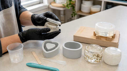 Gloved maker pouring clear resin into a supported silicone jar mould on a tidy craft bench