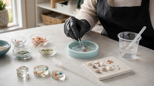 Gloved maker arranging shells, foil and colourful inclusions beside clear resin on a tidy craft bench
