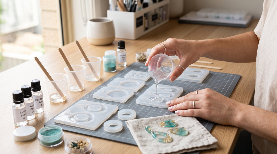 Gloved maker arranging small resin jewellery moulds, inclusions and findings on a tidy daylight workbench