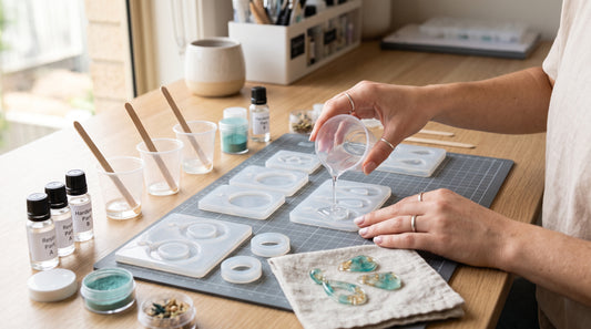 Gloved maker arranging small resin jewellery moulds, inclusions and findings on a tidy daylight workbench