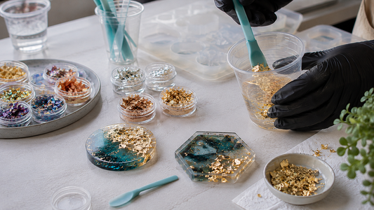 Metallic flakes in small pots beside clear resin, mixing tools and decorative castings on a tidy craft workspace